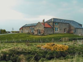 A stone building with a red-tiled roof surrounded by green grass and fencing at The Old Watermill in Beadnell