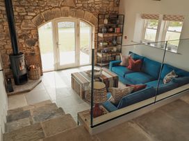A living room with a blue sofa and patterned cushions a striped ottoman a wood stove and stone walls at The Old Watermill in Beadnell