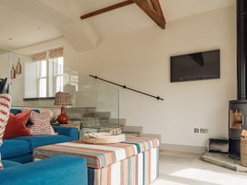 A living room with a blue sofa striped ottoman and wall mounted tv next to a wood stove at The Old Watermill in Beadnell