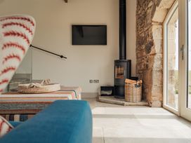 A living room area with a striped ottoman a wood burning stove in a stone corner and a wall-mounted TV at The Old Watermill in Beadnell