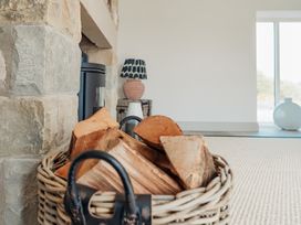 A basket of firewood near a stone fireplace with a lamp and a window in the background at The Old Watermill in Beadnell