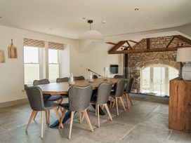 A dining room with a wooden table and chairs near windows and a stone wall at The Old Watermill in Beadnell