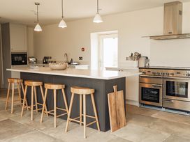 A kitchen with a large island with wooden stools and a stainless steel stove with oven at The Old Watermill in Beadnell