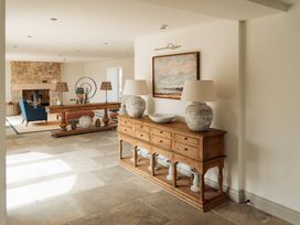 A hallway with a wooden sideboard holding two lamps and decorative items with a painting above it and a living room with a stone fireplace and blue armchair in the background at The Old Watermill in Beadnell