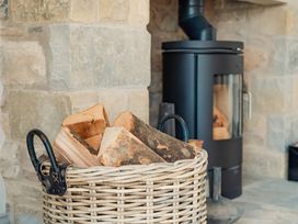 A basket of firewood logs near a black wood stove with stone walls in the background at The Old Watermill in Beadnell