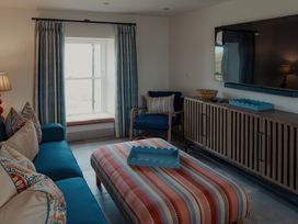 A living room with a blue sofa a patterned ottoman a wooden TV cabinet and a window seat at The Old Watermill in Beadnell