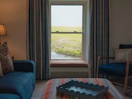 A living room with a window seat overlooking a grassy field and stream at The Old Watermill in Beadnell