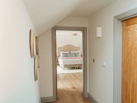 A hallway with wooden flooring leading to a bedroom with a patterned headboard and bed at The Old Watermill in Beadnell