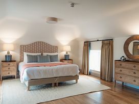 A bedroom with a bed flanked by two bedside tables with lamps and a dresser with a round mirror at The Old Watermill in Beadnell