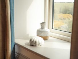 A window sill with a ceramic vase and a white decorative object with curtains at The Old Watermill in Beadnell