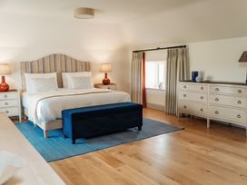 A bedroom with a large bed flanked by two bedside tables with lamps a blue ottoman at the foot of the bed a dresser with decorative items and a window with curtains at The Old Watermill in Beadnell
