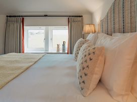 A bed with pillows and a blanket near windows with curtains and a lamp at The Old Watermill in Beadnell