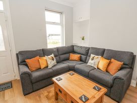 A living room with a grey corner sofa with orange and bee-themed cushions a wooden coffee table and a window at Grace House in Silloth