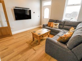 A living room with a grey sectional sofa wooden coffee table mounted flat screen tv and wooden door at Grace House in Silloth