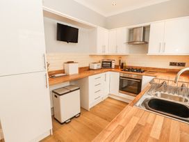 A kitchen with white cabinets wooden countertops a stainless steel sink gas stove oven toaster and mounted television at Grace House in Silloth