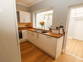 A kitchen with white cabinets wooden countertops a sink and a window with flowers at Grace House in Silloth