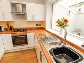 A kitchen with wooden countertops white cabinets a stove and an oven a sink with a dish rack and sunflowers in a vase by a window at Grace House in Silloth