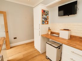 A kitchen corner with white cabinets a wooden countertop a mounted television and a double trash bin at Grace House in Silloth