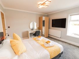 A bedroom with a double bed with yellow pillows and a runner a wardrobe a dressing table a chair and a wall mounted tv at Grace House in Silloth