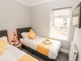 A bedroom with two single beds a bedside table a lamp and a wall-mounted television at Grace House in Silloth