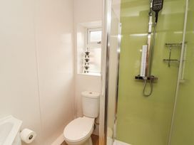 A bathroom with a toilet near a window and a shower with a green wall at Grace House in Silloth