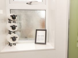 A window sill with three sheep shaped toilet paper holders stacked and a framed Lake District print at Grace House in Silloth