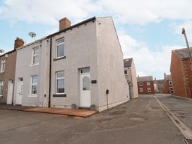 A row of terraced houses on a street with a grey end house and a narrow road beside it at Grace House in Silloth