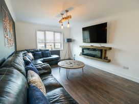 A living room with a black leather corner sofa a round wooden coffee table a wall-mounted TV and an electric fireplace at Ty Copr in Amlwch