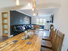 A living room with wooden dining table and chairs a black leather sofa and wall-mounted tv at Ty Copr in Amlwch