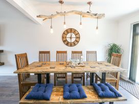 A dining room with a wooden table and chairs with blue cushions and a wooden clock on the wall at Ty Copr in Amlwch
