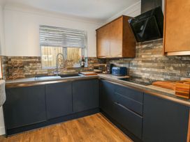 A kitchen with black lower cabinets wooden upper cabinets and a brick backsplash at Ty Copr in Amlwch