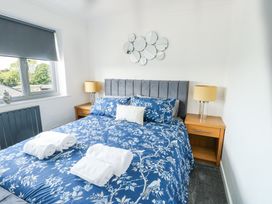 A bedroom with a bed with blue floral bedding two wooden bedside tables with lamps and a window with a closed blind at Ty Copr in Amlwch
