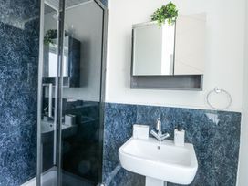 A bathroom with a white sink, a wall-mounted mirror cabinet with a plant on top, and a glass shower enclosure with dark blue marbled walls at Ty Copr in Amlwch