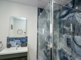 A bathroom with a white sink and a mirror above it with blue marble tiles behind and a glass shower enclosure with blue marble tiles