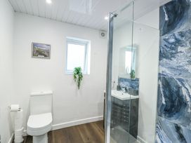 A bathroom with a toilet, a small window, a plant on the window ledge, a framed picture on the wall, a sink with a mirror, and a shower with blue marbled tiles at Ty Copr in Amlwch