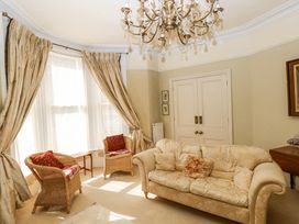 A sitting room with a fabric sofa and two wicker chairs near windows with curtains at Hereford House in Tenby