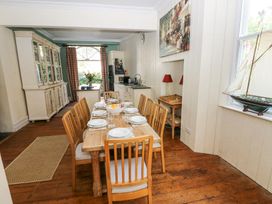 A dining room with a wooden dining table set for eight with plates and glasses a large cabinet an open kitchen area and a model sailboat on the windowsill at Hereford House in Tenby