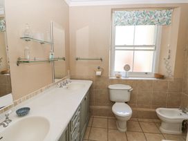 A bathroom with a double sink countertop toilet bidet window with floral valance shelves with bottles and small mirror