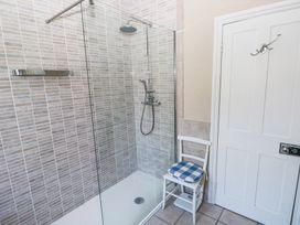 A bathroom with a glass shower enclosure tiled walls and a white chair with a blue checkered cushion near a white door
