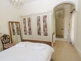 A bedroom with a bed and two rolled towels a wooden chair a full-length mirror built-in wardrobes with floral curtains an arched doorway and a window with curtains at Hereford House in Tenby