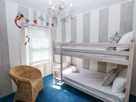 A bedroom with a wooden bunk bed a wicker chair a window with blinds and a chandelier at Hereford House in Tenby