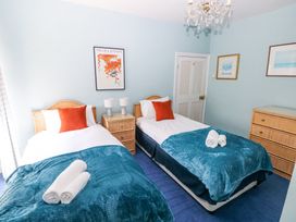 A bedroom with two single beds a nightstand with two lamps a chest of drawers and framed pictures on the wall at Hereford House in Tenby