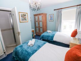 A bedroom with two single beds blue blankets and orange pillows a wooden wardrobe and a window at Hereford House in Tenby