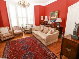 A living room with beige sofa striped armchairs red walls wooden floor and a red patterned rug at Hereford House in Tenby