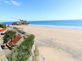 A wide sandy beach with a rocky island and a stone wall with red flowers and greenery overlooking the beach at Hereford House in Tenby