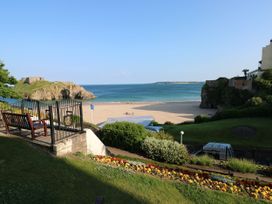 A view of a beach with a gate, bench, flowers, grassy area, and a rocky island in the sea at Hereford House in Tenby
