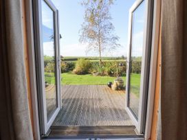 A view through open double doors to a wooden deck and garden with a tree and plants at Artisan Lodge in Longridge