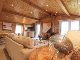 A living room with wooden walls and ceiling a beige sofa a television a coffee table with flowers and a globe at Artisan Lodge in Longridge