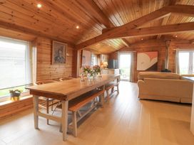 A dining and living area with wooden walls and ceiling a wooden dining table with benches and chairs flowers on the table a beige sofa a television a stove and abstract paintings at Artisan Lodge Longridge