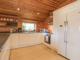 A kitchen with wooden walls and ceiling containing white cabinets a refrigerator oven toaster microwave and open shelves with cups and glasses at Artisan Lodge in Longridge